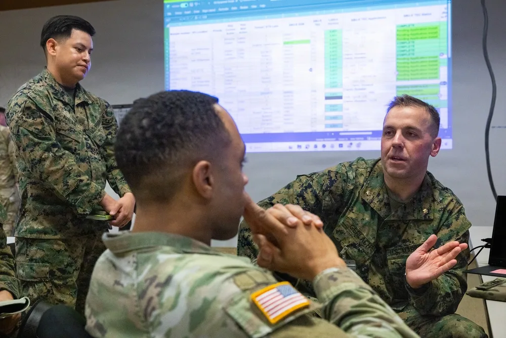 Military personnel in discussion with a large screen displaying data, likely Project Dynamis.