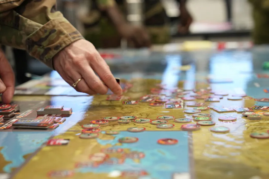Wargame in progress, military personnel strategizing with game pieces on a map.