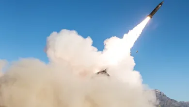 Missile launching with smoke plume against blue sky and desert landscape.