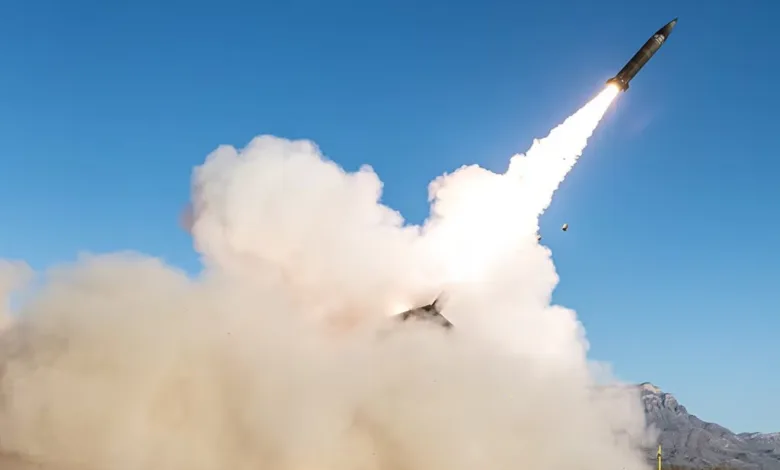 Missile launching with smoke plume against blue sky and desert landscape.