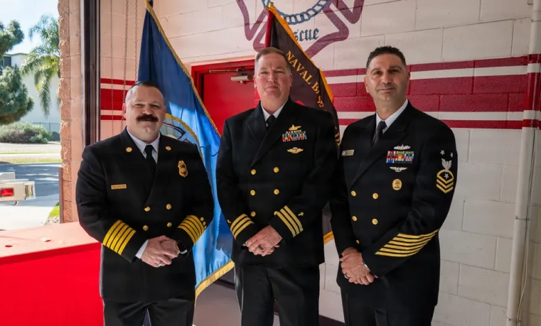 Three naval officers in uniform stand in front of a fire station backdrop.