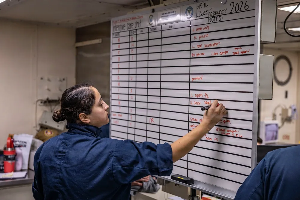 Navy medic updates patient notes on USS Iwo Jima's Intensive Care Unit whiteboard.