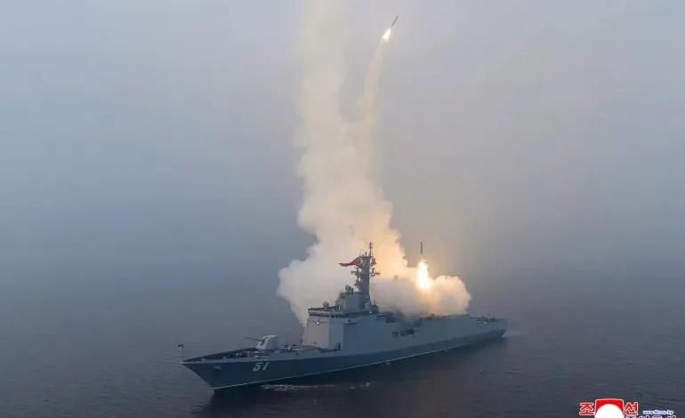 North Korean warship firing missile in naval exercise, smoke and sea visible.