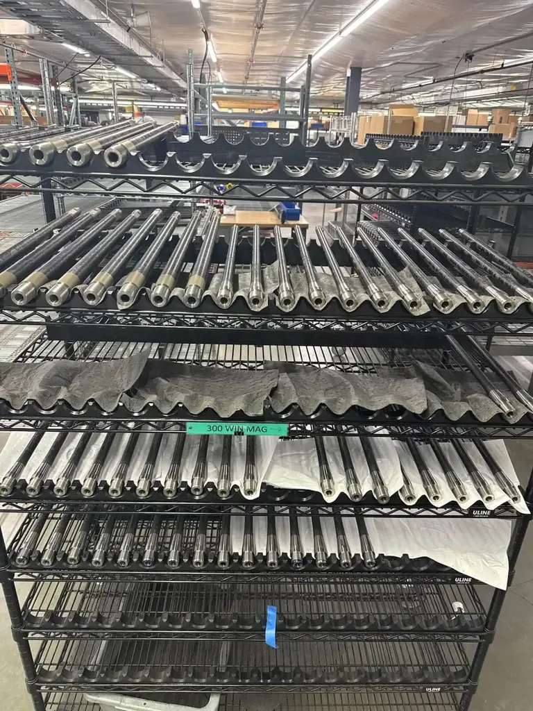 Rifle barrels on shelves, some labeled "300 WIN MAG". Manufacturing or gunsmithing setting.