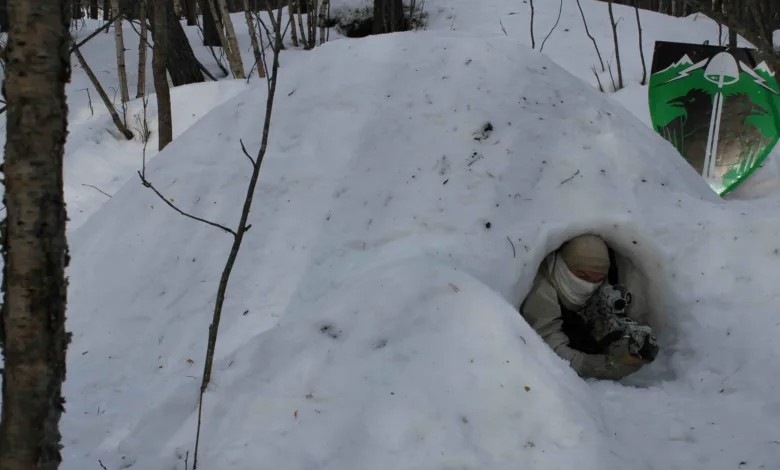 Camouflaged sniper in snow shelter with rifle, winter warfare.