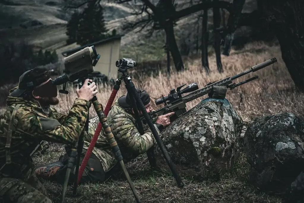 Two snipers in camouflage gear using rifles and optics in a field setting.