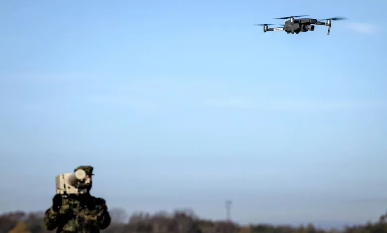 Soldier aims drone jammer at drone in flight. Anti-drone warfare.