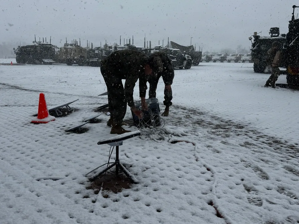 Soldiers working on equipment in snowy field with military vehicles in background. Project Dynamis.