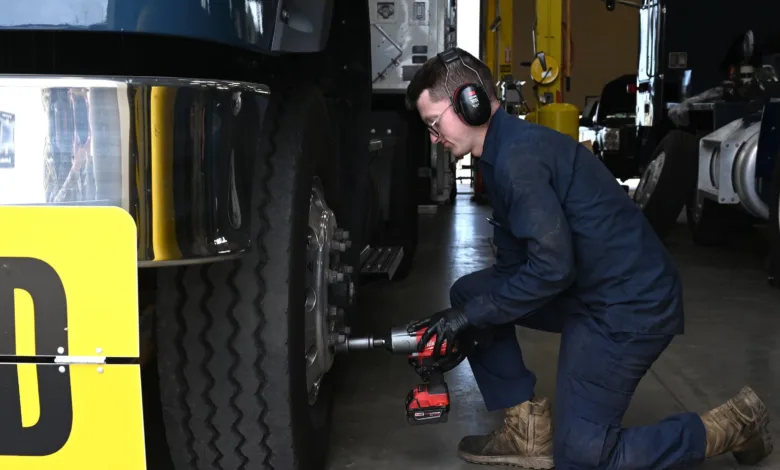 Mechanic using impact wrench on truck tire in garage, safety gear