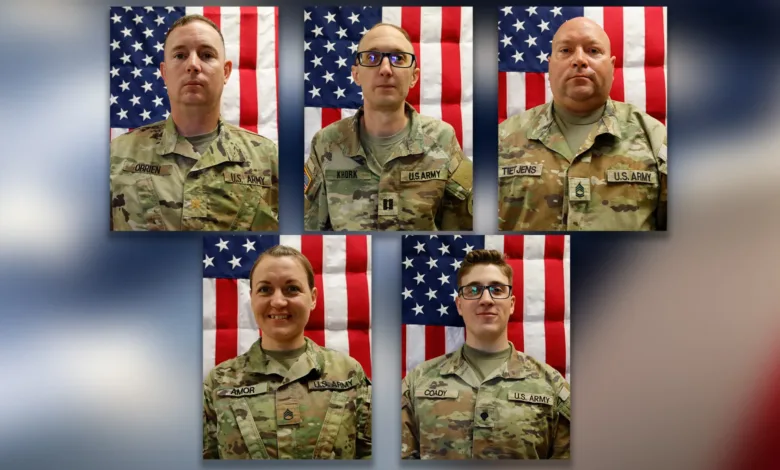 Group portrait of five U.S. Army soldiers in uniform against American flags.