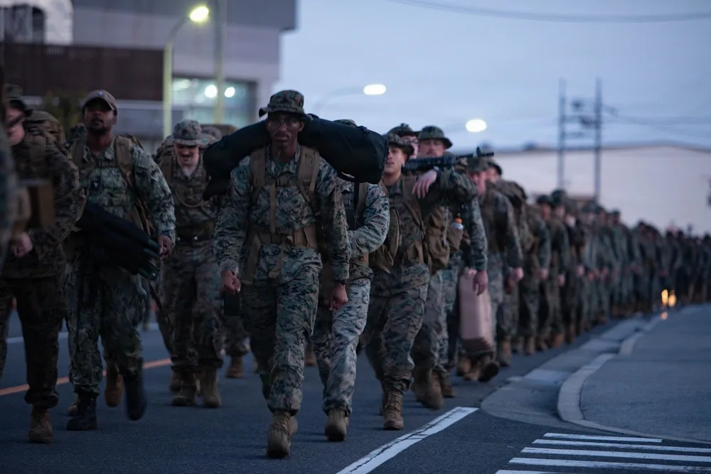 US Marines in camouflage uniforms march with gear, early morning.