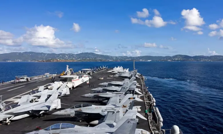 US Navy aircraft carrier with F/A-18 Super Hornets on deck near coastline.