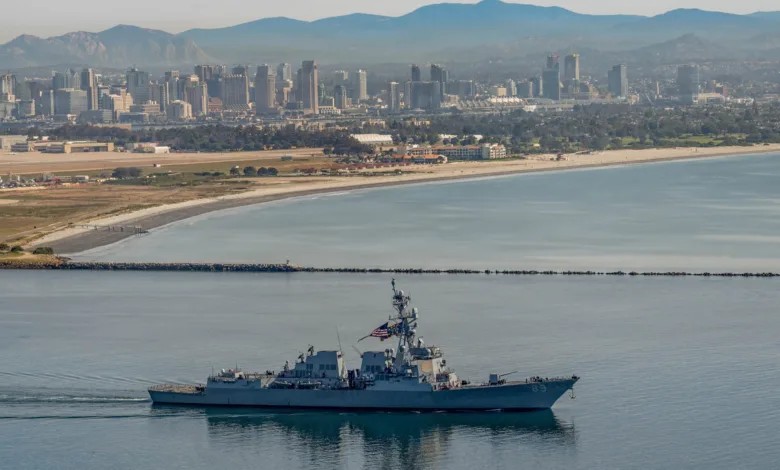 US Navy destroyer sailing near San Diego skyline.