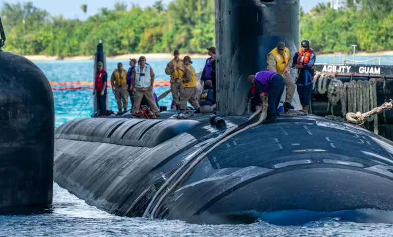 US Navy submarine with crew members on deck at Guam, "AGILITY GUAM" visible.