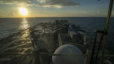 US Navy warship at sea during sunset with gun mounts visible.