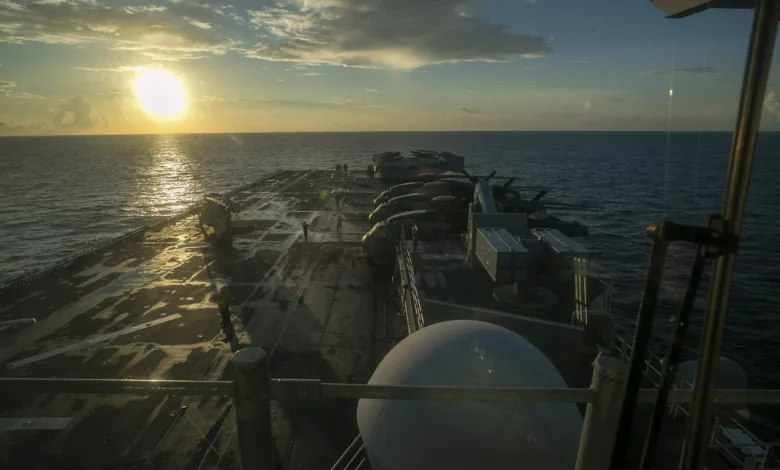 US Navy warship at sea during sunset with gun mounts visible.