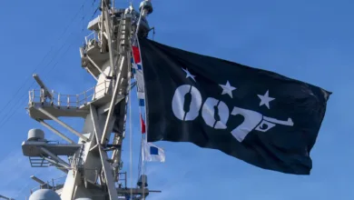 Black 007 flag with gun hoisted on ship mast against blue sky.