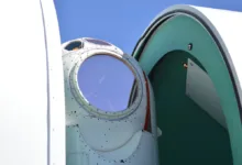 Close-up of a circular aircraft cockpit window with a blue sky reflection.
