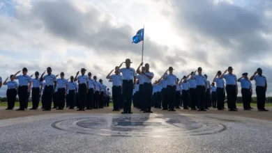 Airmen in formation salute during an outdoor ceremony with a flag.