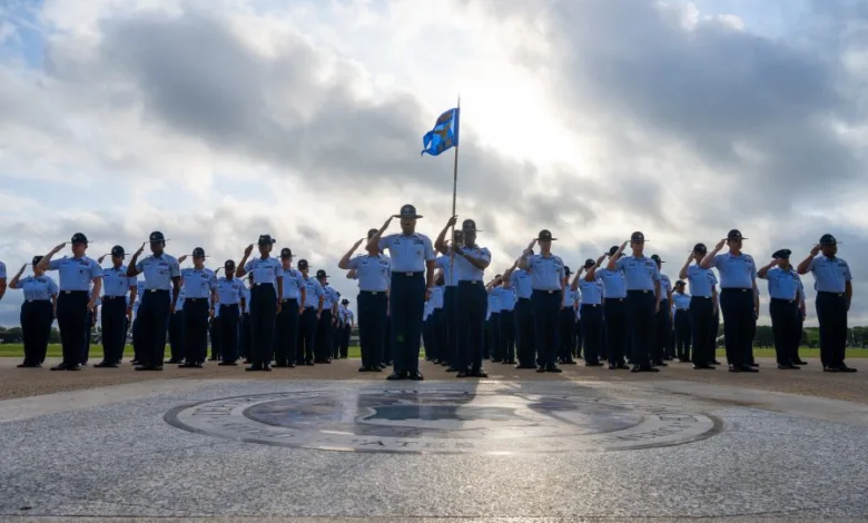Airmen in formation salute during an outdoor ceremony with a flag.