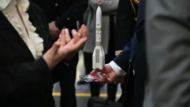 Model rocket held by man in suit, with people in background