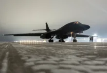 B-1B Lancer bomber on a foggy tarmac at night with lights in the background.