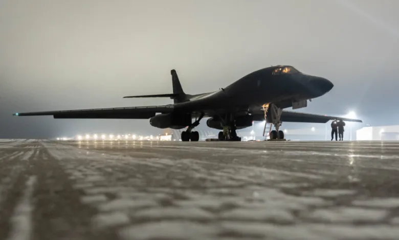 B-1B Lancer bomber on a foggy tarmac at night with lights in the background.
