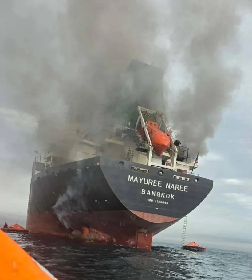 Burning cargo ship Mayuree Naree Bangkok at sea, smoke billowing, life rafts deployed.