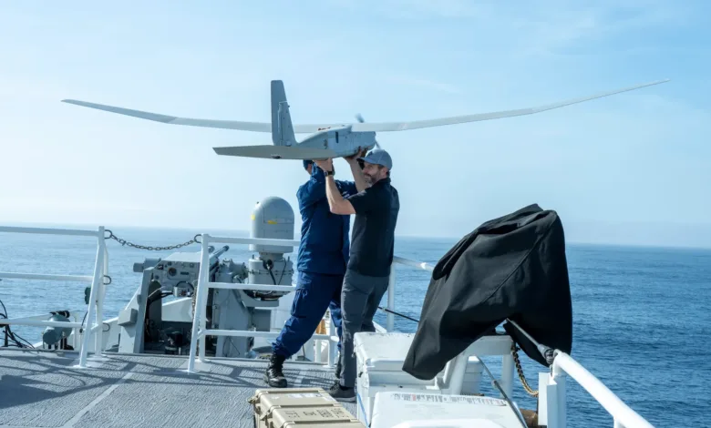 Two men preparing a drone for launch on a ship at sea.