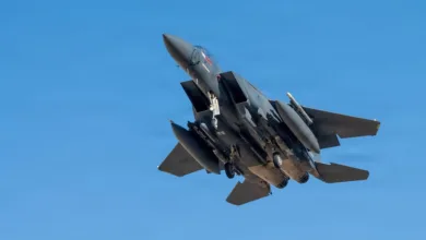F-15 Eagle fighter jet with landing gear down against a clear blue sky.