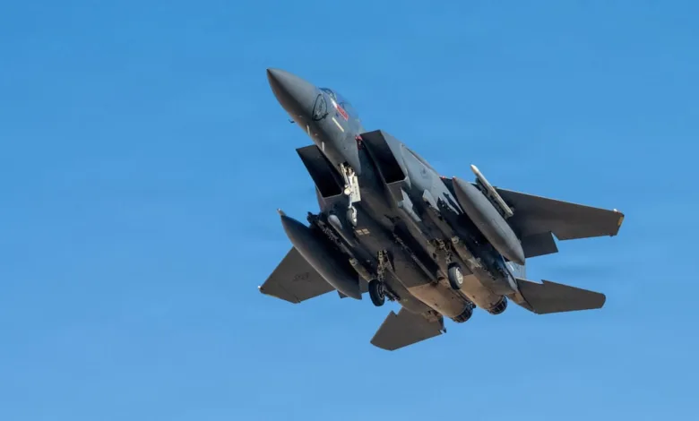F-15 Eagle fighter jet with landing gear down against a clear blue sky.