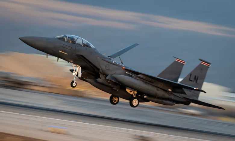 F-15 Eagle fighter jet taking off with afterburners engaged, desert backdrop. Tail code LN visible.