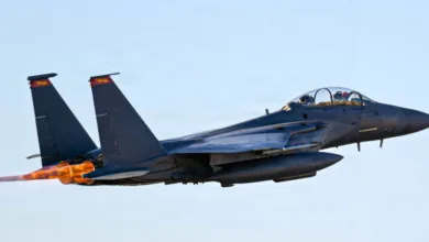F-15 Eagle fighter jet taking off with afterburners engaged, blue sky background.
