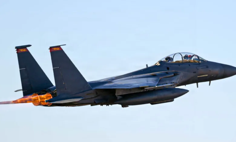 F-15 Eagle fighter jet taking off with afterburners engaged, blue sky background.