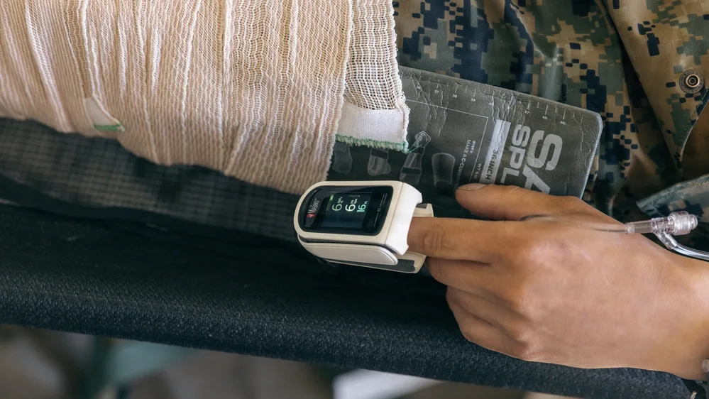 Injured person with bandage and pulse oximeter showing 66. Simulated casualty evacuation training.
