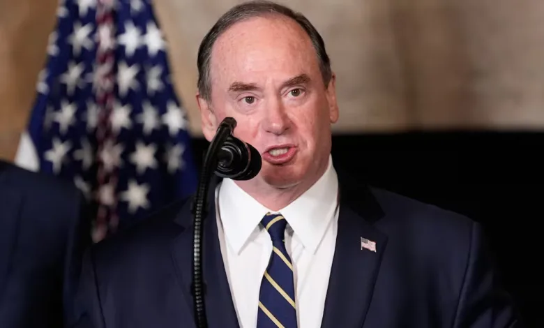 Man in suit speaking at a podium with American flag behind him