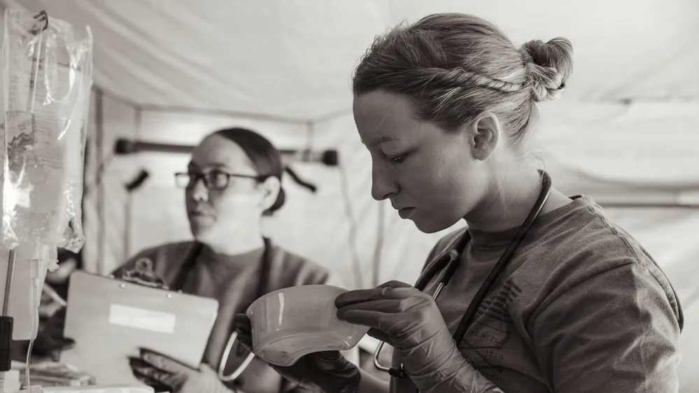 Medics training casualty evacuation; one holds a bowl, another takes notes.