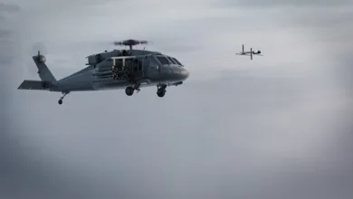 Military helicopter firing missile at drone in flight, gray sky background.