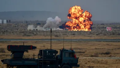 Missile launch system vehicle in foreground, large explosion in background at military exercise.