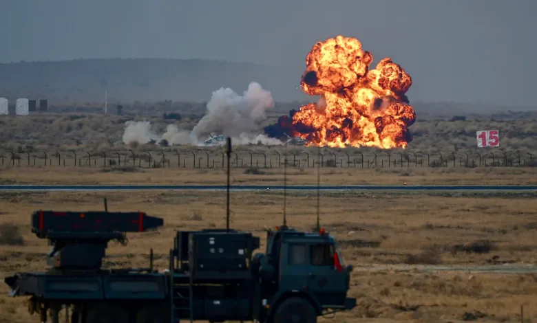 Missile launch system vehicle in foreground, large explosion in background at military exercise.