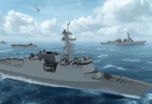 Modern naval frigates and cargo ships sail in formation on the ocean under a cloudy sky.