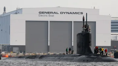 Submarine at General Dynamics Electric Boat shipyard with crew on deck.