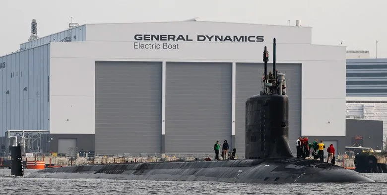 Submarine at General Dynamics Electric Boat shipyard with crew on deck.