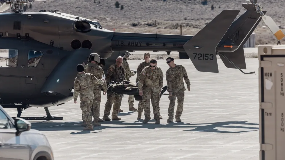 US Army personnel carrying a stretcher to a helicopter on a tarmac.