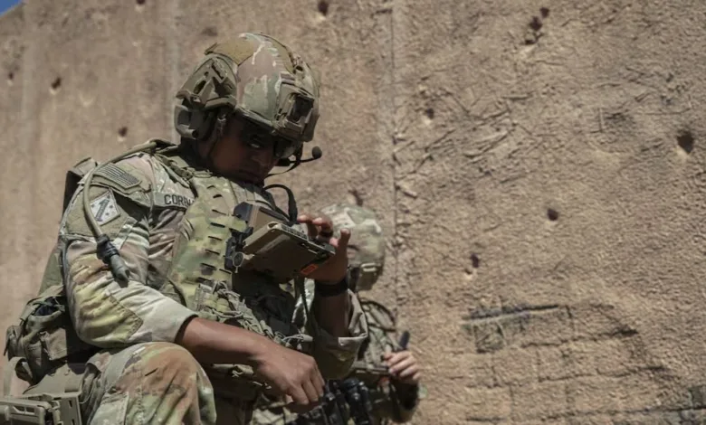 U.S. Army soldier in tactical gear adjusts equipment near a wall.