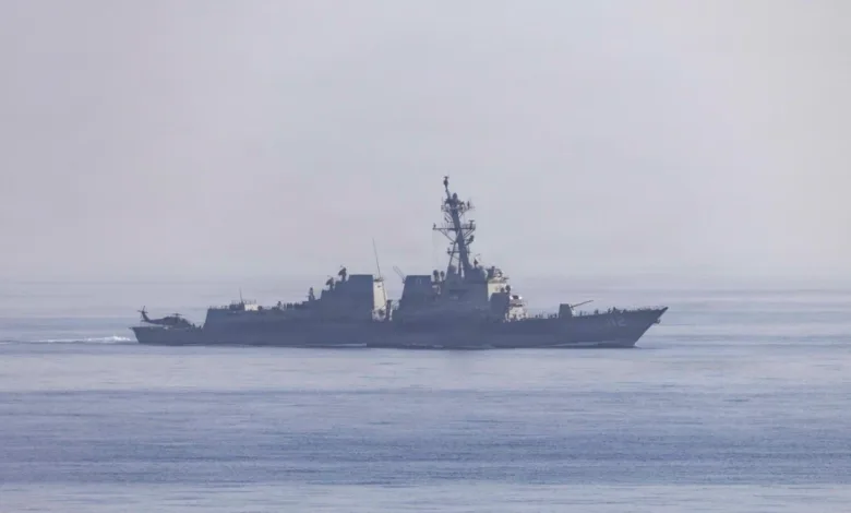 US Navy Arleigh Burke-class destroyer sailing on the ocean with a helicopter on the deck.