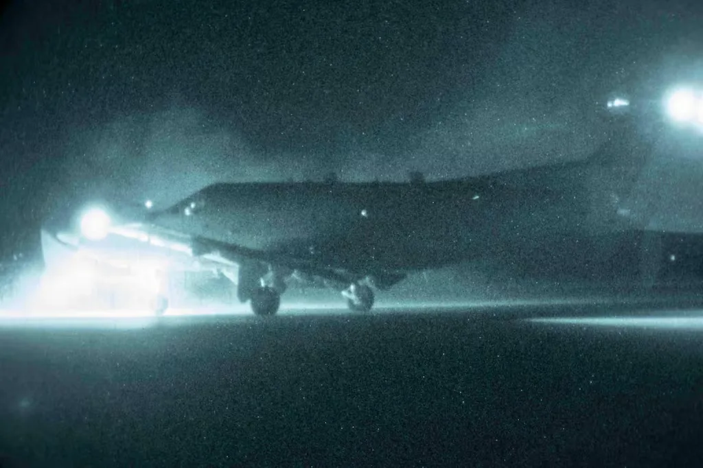 Airplane landing at night with bright landing lights illuminating the runway.