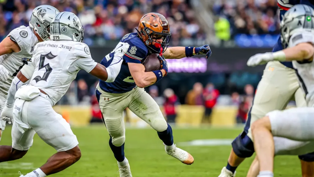Army player with ball runs past defenders during a football game.