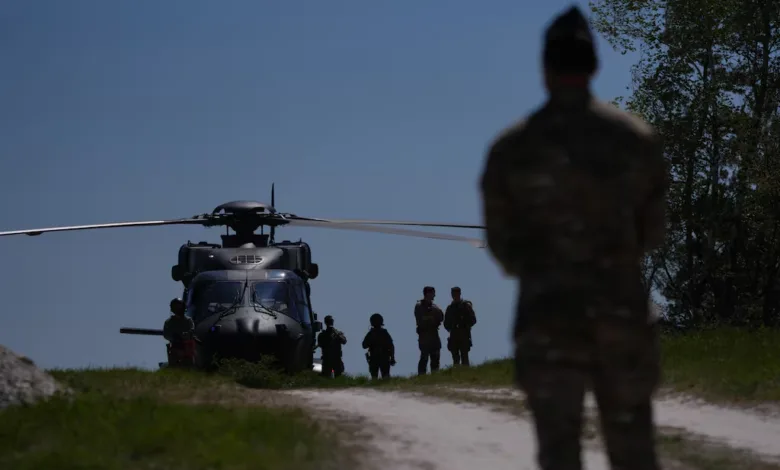 Military personnel stand near a Black Hawk helicopter on a grassy field.