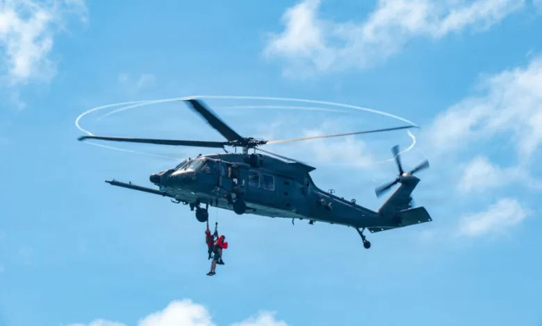 Black helicopter with two people hanging from a rope in a blue sky